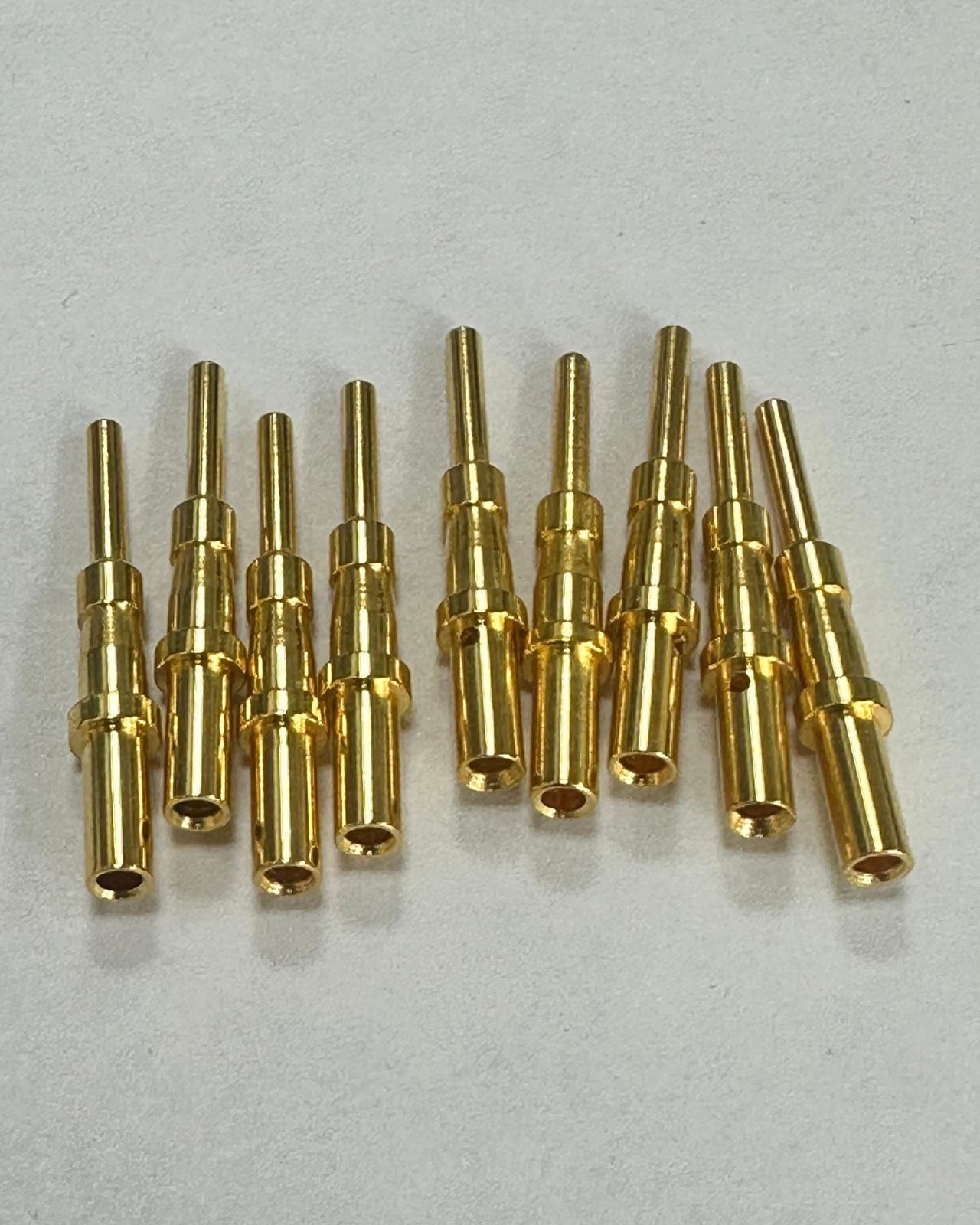 Nine gold-plated connector pins on white paper